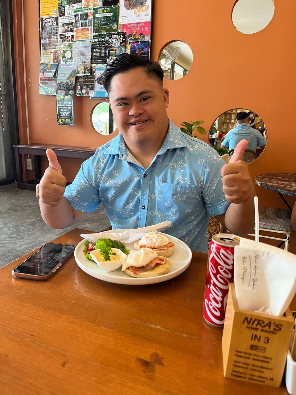 Super Mark smiling and giving two thumbs up in a cafe